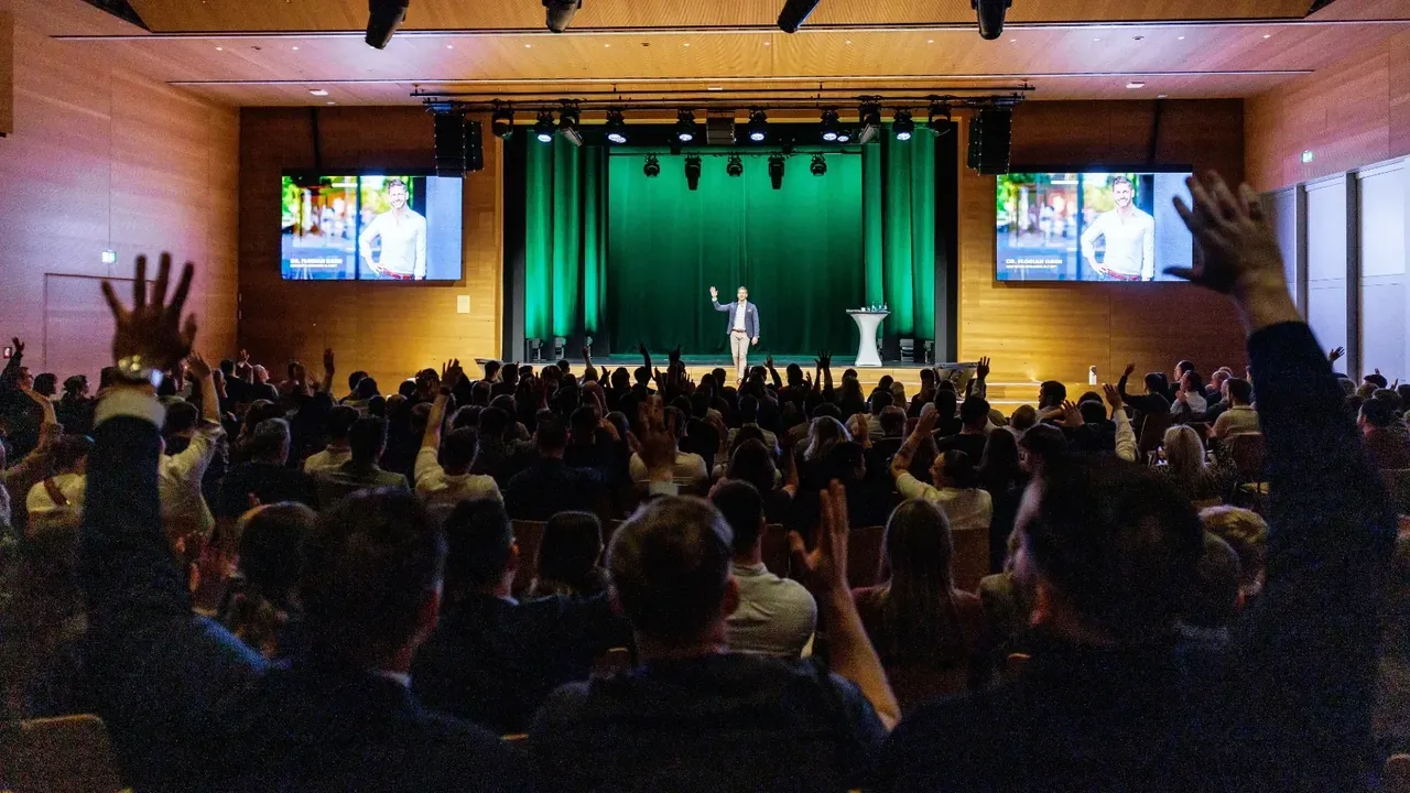 Audience members raise hands in response to the keynote speaker on an Amsterdam stage
