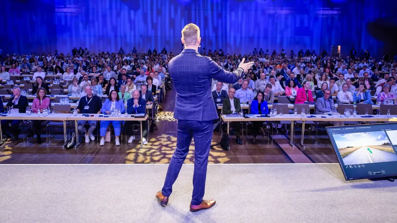 Rows of conference delegates face the stage during a keynote by Dr. Florian Ilgen